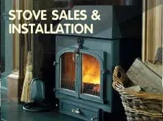 Stove sales and installation: a lit cast iron stove beside a log basket