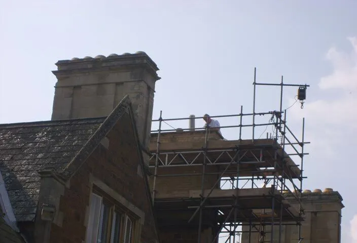 Scaffolding and a roof platform around a tall stone chimney stack on a period building