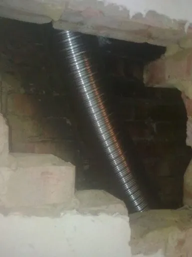 Flexible metal flue liner being fitted through an opened-up chimney breast