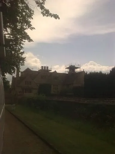 Country house with work under way on its chimneys, seen across the lawn