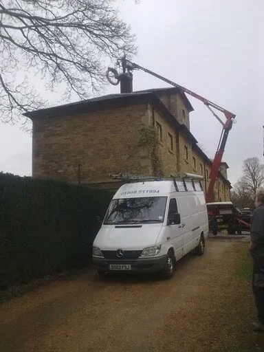 Our van parked beside a house while a cherry picker reaches the chimney
