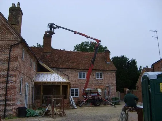 Cherry picker raised to the chimney of a red brick house