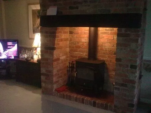 Wood burning stove in a brick inglenook under a dark timber beam