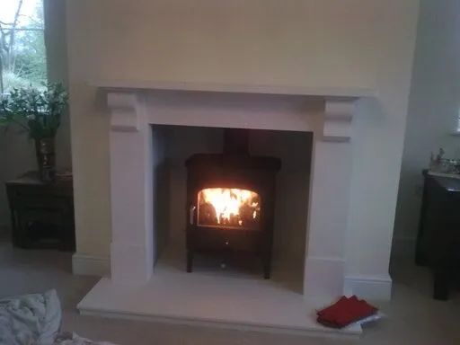 Lit stove inside a pale stone fireplace surround